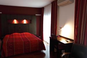 a bedroom with a red bed and a desk and a window at Hôtel la Scala in Pithiviers