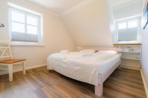 a white bedroom with a bed and two windows at Haus Oase in Sankt Peter-Ording