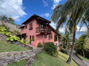 a pink house with a balcony and a palm tree at Casa Yacht Club in Ilhabela