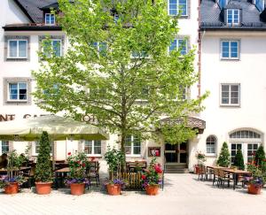 Un hotel con mesas y sillas y un árbol frente a un edificio. en Hotel Weisses Ross, en Memmingen