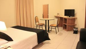 a hotel room with a bed and a table and a television at Hotel Ouro Lavras in Lavras