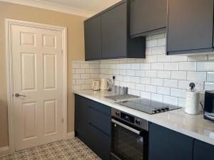 La cuisine est équipée de placards bleus et d'un four avec plaques de cuisson. dans l'établissement 3-Bed Home Close to City Centre, Stadium & Baltic, à Newcastle upon Tyne