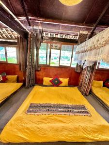 a bedroom with two beds with yellow sheets and windows at Đá Nhớ Homestay in Mèo Vạc