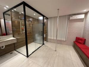baño con ducha de cristal y sofá rojo en Motel Orion - Belo Horizonte, en Belo Horizonte