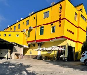 a yellow building with tables and umbrellas in a parking lot at London Restaurant Hotel in Kukës