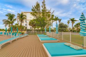 a row of blue mats on a deck with chairs and umbrellas at Ocean View Top-Floor Sunset Vistas Condo! in St Pete Beach