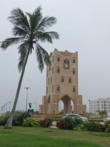 un edificio con una torre de reloj y una palmera en صلاله, en Salalah