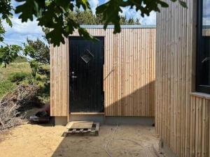 een houten gebouw met een zwarte deur en een bankje bij HS001-Henne-Enebaervej-6 in Henne Strand
