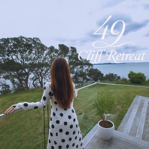 a woman in a polka dot dress standing on a balcony at 49 Cliff Retreat in Whangaparaoa