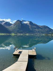 a dock with two benches on a lake with a mountain at Vollsnes Glamping in Hjelle