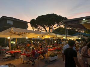 Eine Gruppe von Menschen sitzt an Tischen mit Sonnenschirmen. in der Unterkunft Hotel Maxim in Caorle