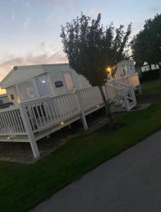 a white house with a porch and a tree at 27 Ivy Close in Mablethorpe