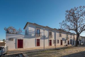 a white building with red doors and a tree at Dona Ana House in Tavira