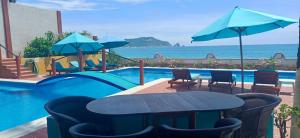 a table and chairs next to a swimming pool with the ocean at La Paloma Oceanfront Retreat in San Patricio Melaque