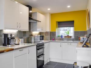 a kitchen with white cabinets and a yellow wall at Dutch Barn One - Uk12872 in Brynkir +9 photos