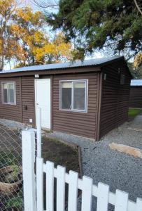 a small brown cabin with a white fence at Las Casitas de Don Hugo in General Belgrano