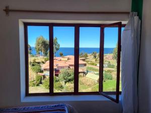 a bedroom window with a view of a house at kaypi rosas wasi Amantani in Ocosuyo