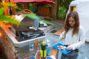 a woman preparing food in front of a grill at North Cascades Glamping with Hot-tub and Outdoor Kitchen in Rockport +28 photos