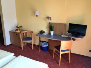 a hotel room with a desk with a television and chairs at Hotel Ambiente in Halberstadt
