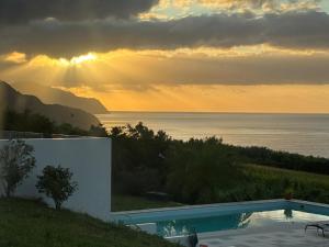 a sunset over the ocean with a swimming pool at Grande Mar Villa in Ponta Garça