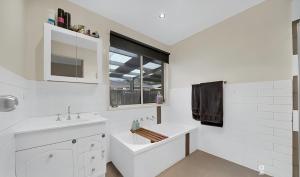 Un baño blanco con lavabo y ventana en Its Hugo Cottage, en Truganina