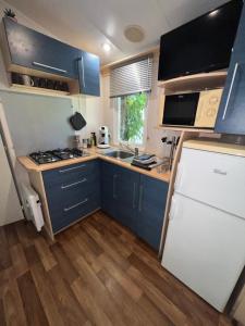 eine kleine Küche mit blauen Schränken und einem weißen Kühlschrank in der Unterkunft Le Gewurz - Bungalow climatisé avec TV pour 5 in Boofzheim