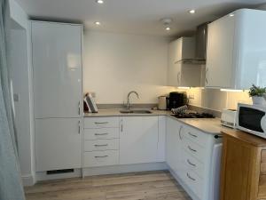 a white kitchen with a sink and a microwave at Cotswold studio with kitchen & patio in Witney