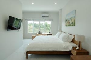 a white bedroom with a large bed and a television at no 185 hostel in Ban Pak Nam Pran