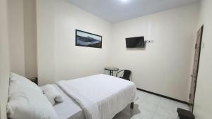 a white bedroom with a bed and a tv at Huis TANTI Homestay Jember in Wirolegi