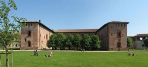 un grand bâtiment en briques avec des gens assis dans l'herbe dans l'établissement Corte 31, à Vigevano