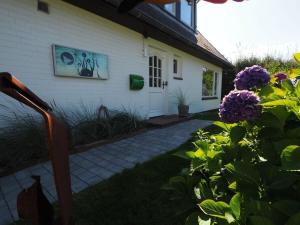 une maison blanche avec des fleurs violettes devant elle dans l'établissement Süderhof Apartment 1, à Keitum