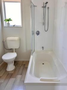 a white bathroom with a toilet and a bath tub at 3 Bedroom Apartment next to Blake Park in Mount Maunganui +4 photos