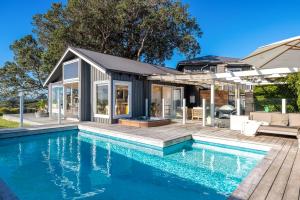 a house with a swimming pool in front of a house at Palm Beach Retreat - Be My Guest Waiheke in Waiheke Island