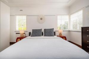 a white bedroom with a large bed and two windows at Deco Days - Prahran in Melbourne