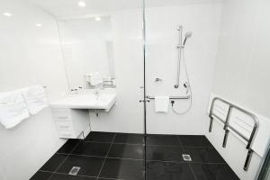 ein weißes Bad mit einer Dusche und einem Waschbecken in der Unterkunft Oaks Gladstone Grand Hotel in Gladstone