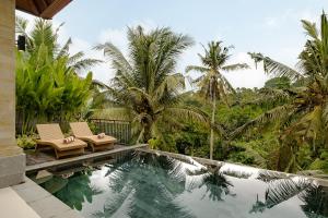 a swimming pool with two chairs and palm trees at Yanyan Resort Ubud in Ubud