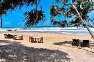 a table and chairs on a beach with the ocean at Vaaru Beach Villa in Kosgoda