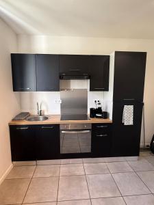 a kitchen with black cabinets and a sink at T2 proche Techn'hom in Cravanche +18 photos