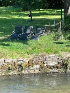 three empty benches sitting on the grass near the water at Chambres de hôte les moulin la paille in Veyre-Monton