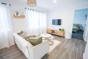 Una sala de estar con un sofá blanco y un televisor. en Pink Muse, 3 Mins To Ettalong Beach, en Ettalong Beach