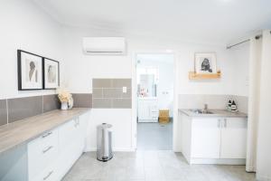Una cocina blanca con gabinetes blancos y un fregadero. en Pink Muse, 3 Mins To Ettalong Beach, en Ettalong Beach