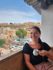 a woman sitting on a balcony holding a cup of coffee at Hostel The Dara in Jaisalmer