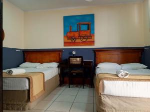 a room with two beds and a desk and a painting at Hotel Plaza Cosiguina in Chinandega