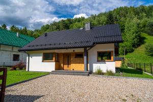 a small white house with a black roof at Domek na Duzynie in Ochotnica Górna