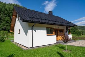a small white house with a black roof at Domek na Duzynie in Ochotnica Górna