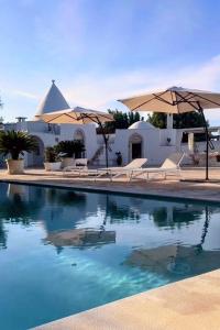ein Pool mit zwei Sonnenschirmen und ein Gebäude in der Unterkunft Trullo il Gelso with Private Salt Water Infinity Pool and Jacuzzi inside in San Michele Salentino