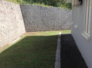 a backyard with a brick wall and a grass yard at Les terrasses de Maëlle II in Rivière-Salée