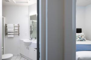 a white bathroom with a sink and a bed at Quest On The Terrace Serviced Apartments in Wellington +25 photos