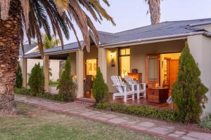 una casa con un portico con sedie bianche e una palma di La Plume Boutique Hotel & Spa a Oudtshoorn