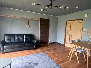 a living room with a black leather couch and a table at ペコレラ学舎 Teacher House in Yakumo